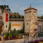 Castelo de entrada do parque Mini Mundo em Gramado, com arquitetura em estilo medieval, bandeiras vermelhas nas torres e visitantes caminhando na entrada, em um dia ensolarado.
