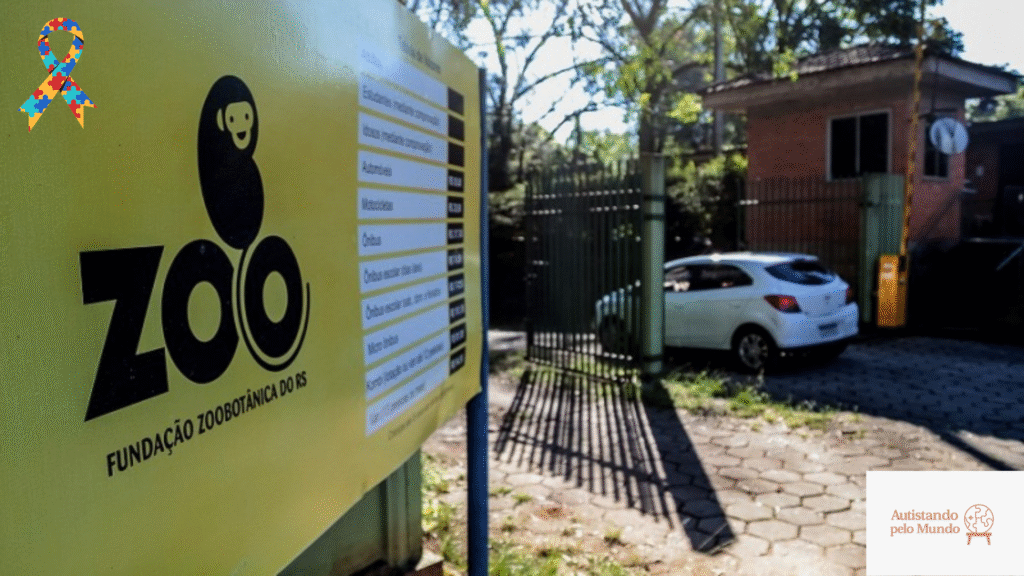 Placa amarela com o logo “ZOO” na entrada do Zoológico de Sapucaia, ao lado de um portão de ferro; árvores e um carro branco ao fundo.