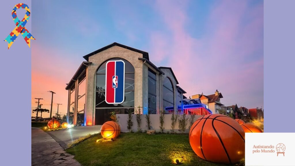 Fachada do NBA Park Gramado ao entardecer com bolas de basquete decorativas iluminadas no jardim e logotipo da NBA na entrada do parque temático
