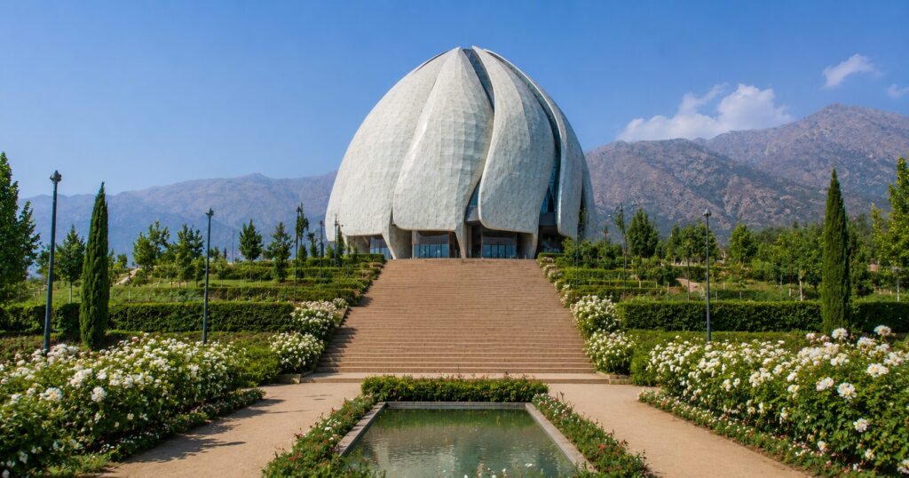 Vista frontal do Templo Bahá'í em Santiago, no Chile, cercado por jardins e pela Cordilheira dos Andes ao fundo.